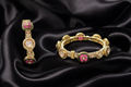 A gold Kundan-style bangle and matching ring set with clear uncut stones and pink and green enamel floral accents, displayed on draped black satin fabric.