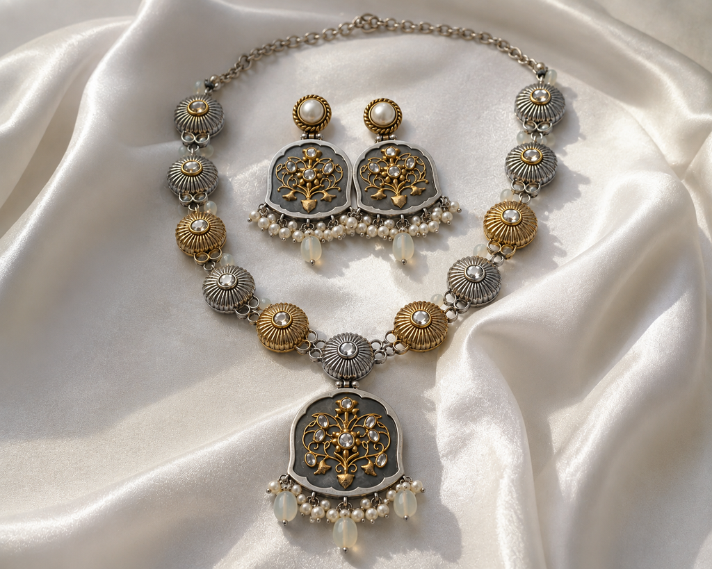 An ornate jewelry set featuring a necklace and matching earrings with silver and gold-toned filigree details, white faux pearls, and clear teardrop beads, arranged on draped white satin fabric.