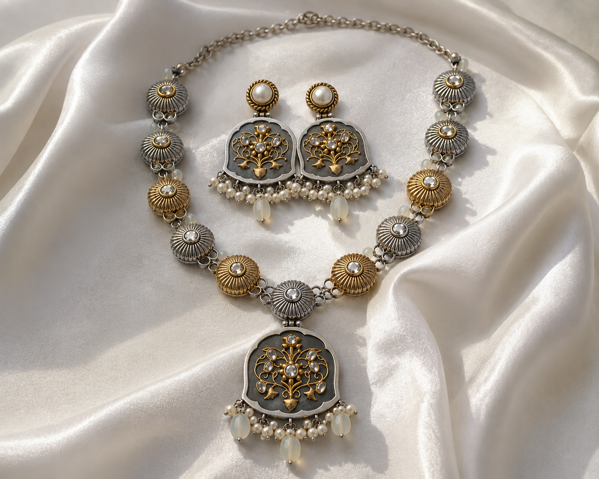 An ornate jewelry set featuring a necklace and matching earrings with silver and gold-toned filigree details, white faux pearls, and clear teardrop beads, arranged on draped white satin fabric.