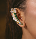 A close-up of a model's ear wearing a green pea pod ear cuff. The ear cuff features a gold-tone metal frame, green enamel, white faux pearls, and clear rhinestones forming a bow at the top.