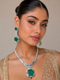 A close-up lifestyle shot of a model wearing an emerald and diamond jewelry set, featuring a statement necklace with a large emerald pendant and matching emerald and diamond drop earrings, paired with a gold embroidered outfit.